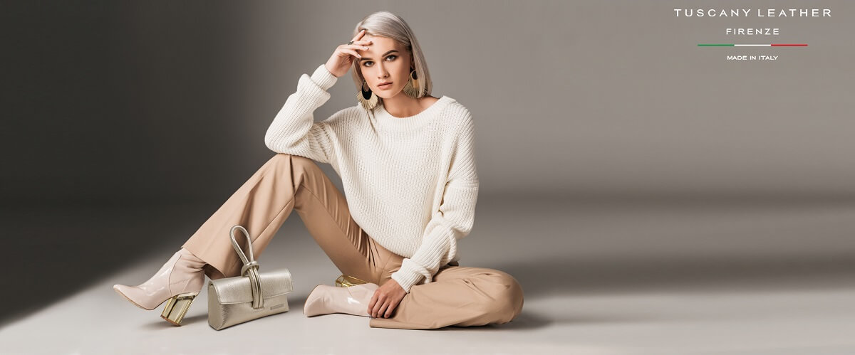 Woman in a cream jumper and beige trousers beside a small metallic leather handbag